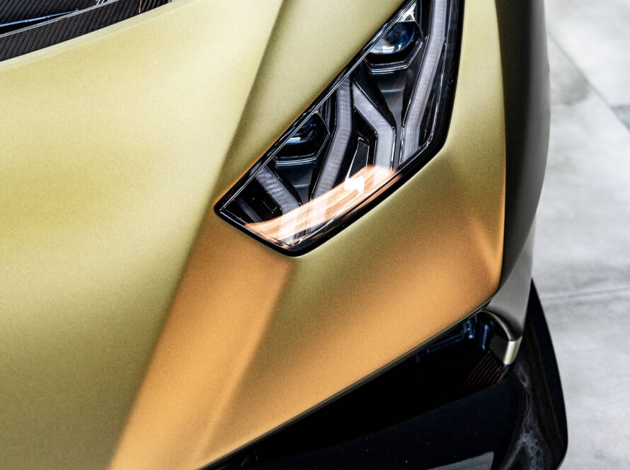 Detailaufnahme des aggressiven LED-Scheinwerfers eines mattgold folierten Lamborghini.