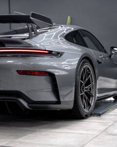 Seitliches Profil des Hecks eines Porsche 911 GT3 in Grau mit Spiegelungen der Werkstattbeleuchtung auf dem Lack.
