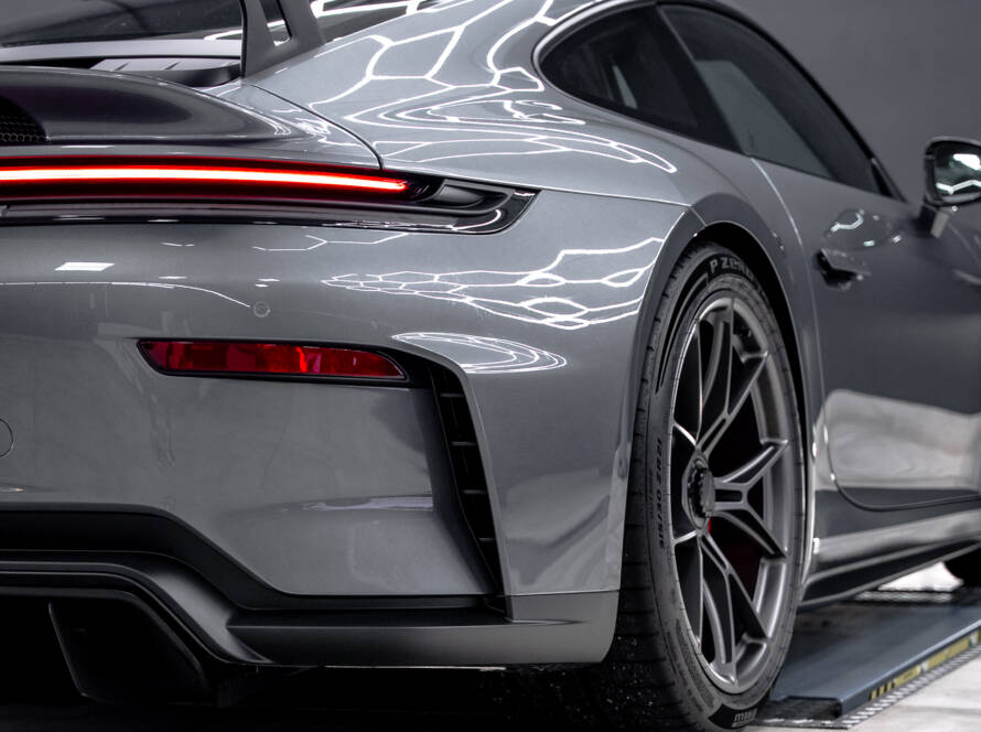 Seitliches Profil des Hecks eines Porsche 911 GT3 in Grau mit Spiegelungen der Werkstattbeleuchtung auf dem Lack.