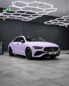 Dreiviertelansicht eines fliederfarbenen Mercedes CLA von vorne in einer modern beleuchteten Halle.